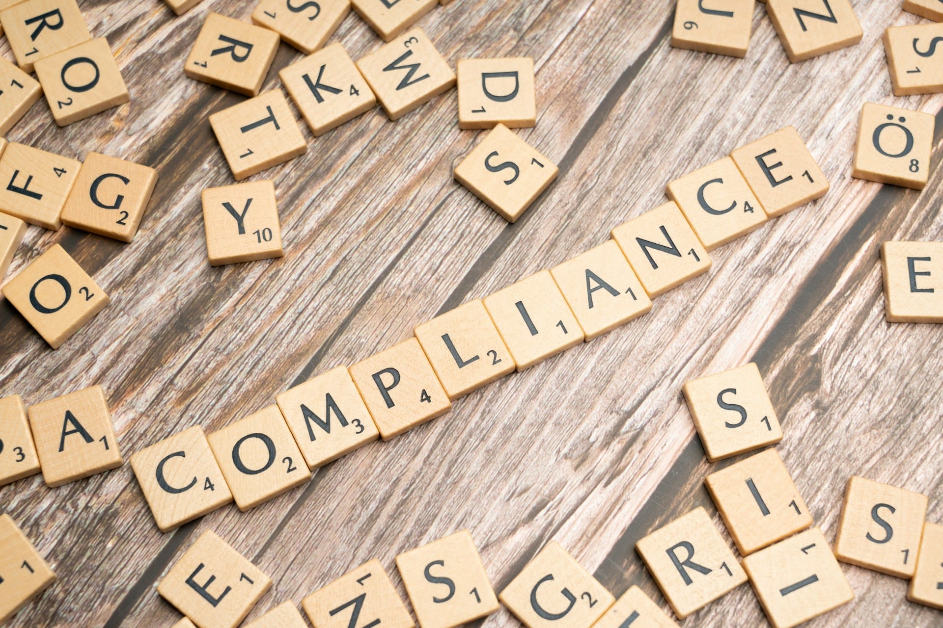 the word "compliance" is spelled out on a scrabble board